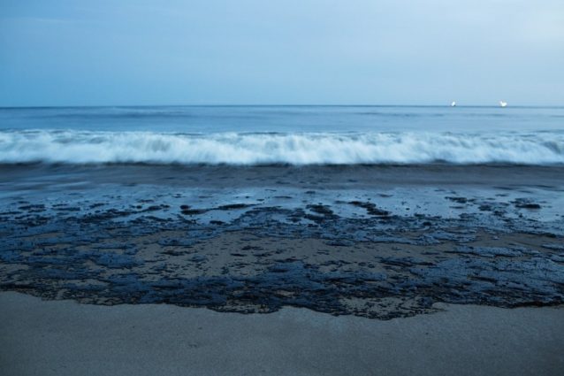 水平線に海洋掘削ドリルが光るなか、原油がビーチへと流れていく。Photo: Erin Feinblatt