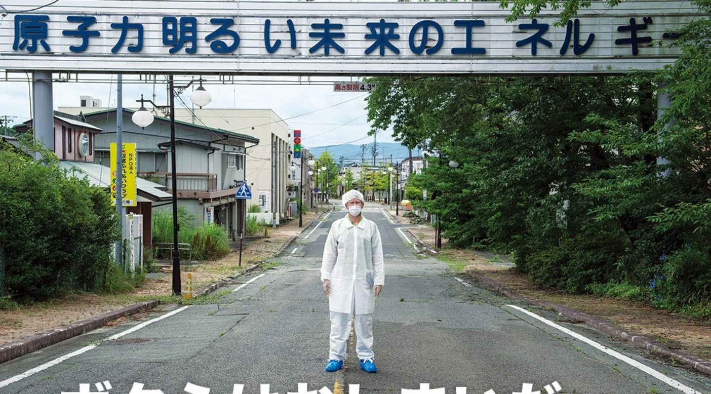 ひとけのない双葉町で、スローガンが掲げられた看板の前に立つ、防護服とマスクを身に着けた人。2011年3月、福島第一原子力発電所の事故により全町民が避難した。このスローガンは今、皮肉にも原子力への依存の危険性を思い出させている。Photo: Arkadiusz Podniesinski