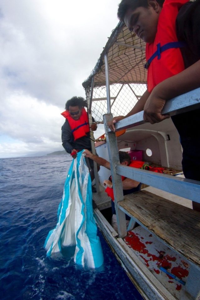 近隣の島にある学校を訪れる途中、海に漂う空気の抜けた子供用プールを拾い上げる乗組員レックス・ロケニ。Photo: John Bilderback