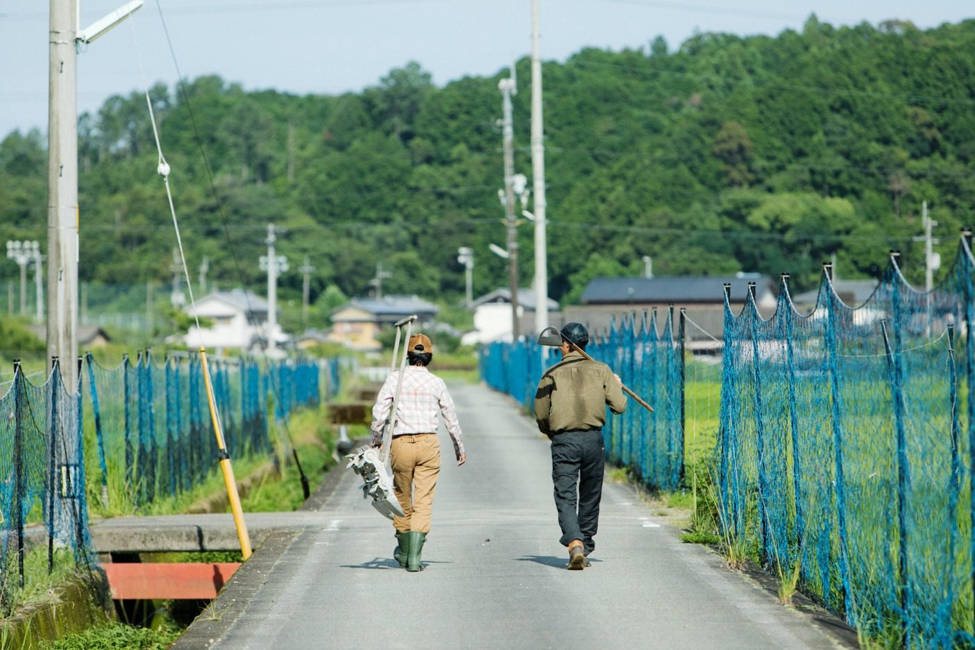夫婦で仲良く田んぼに向かう。美子さんが持っているのは、昔ながらの手押しの除草機。この時期に欠かせない農具の一つだ。写真:五十嵐 一晴