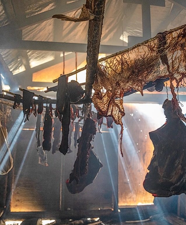 カリブーの肉は燻し小屋に吊るされ、それから冬のために冷凍庫に保存される。若者は長老たちから、冬を過ごすための食料の準備と保存の方法を学ぶ。 Photo: Keri Oberly