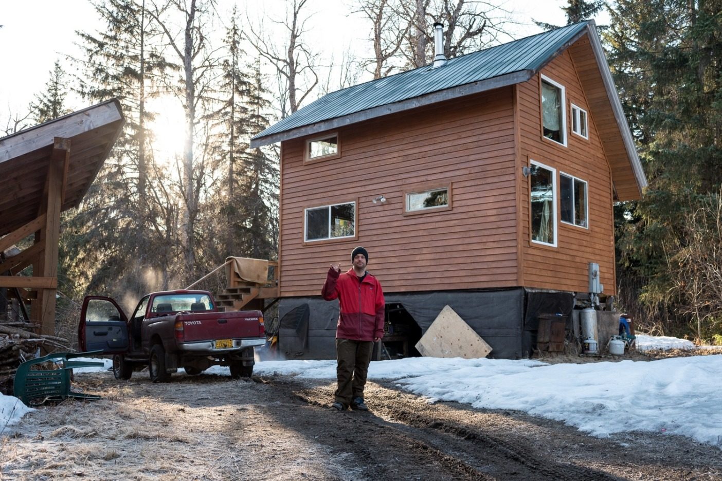 アラスカ州ヘインズの郊外42キロメートルの場所にある自宅の前に立つベル。シンプルな2階建ての家には、屋外コンポストトイレ、暖房用のウッドストーブ、調理用のプロパンコンロ、キッチンに設置するオンデマンド式のシャワーがある。Photo:Colin Wiseman