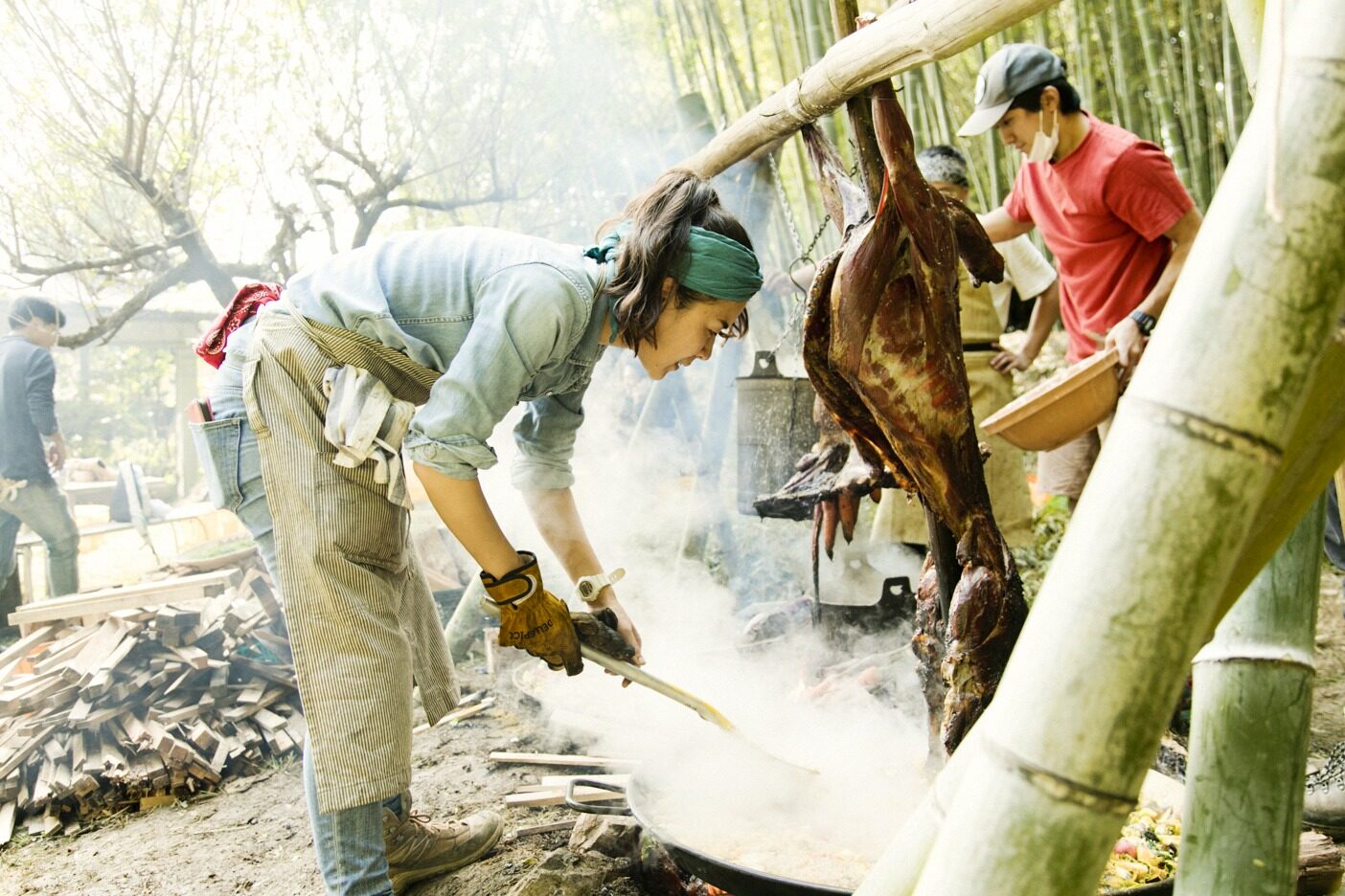 焚き火でシカ肉のグリルとパエリアを仕上げる。竹のアーチは、三上さんと仲間たちが「Ome Farm」敷地内の竹林から竹を切り出し、加工したもの。薪は三上さんが近隣をまわってかき集めた端材だ。写真 : 五十嵐 一晴